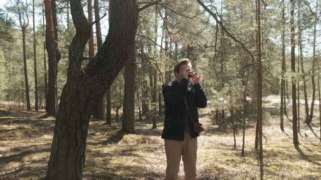 A young blond photographer takes pictures in the woods with a film camera. A photographer in a sunny forest. . High quality 4k footage
