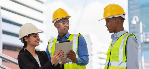 black engineer manager with glasses and helmet working with businesswoman on tablet and looking at black labor engineer. group of engineer working at construction site outside building in city