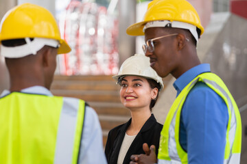 caucasian businesswoman with helmet in black suit happy working with black engineer colleague. group of engineer working at construction site outside building in city