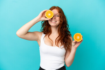 Teenager redhead girl isolated on blue background in swimsuit and holding an orange