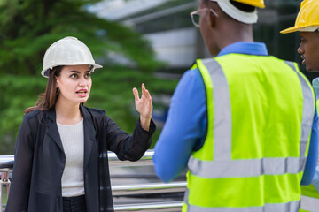 angry emotion of caucasian manager woman in black suit angry black engineer about work mistake. group of engineer working at construction site outside building in city