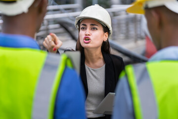 caucasian manager woman in black suit with helmet angry black engineer about work mistake. group of engineer working at construction site outside building in city