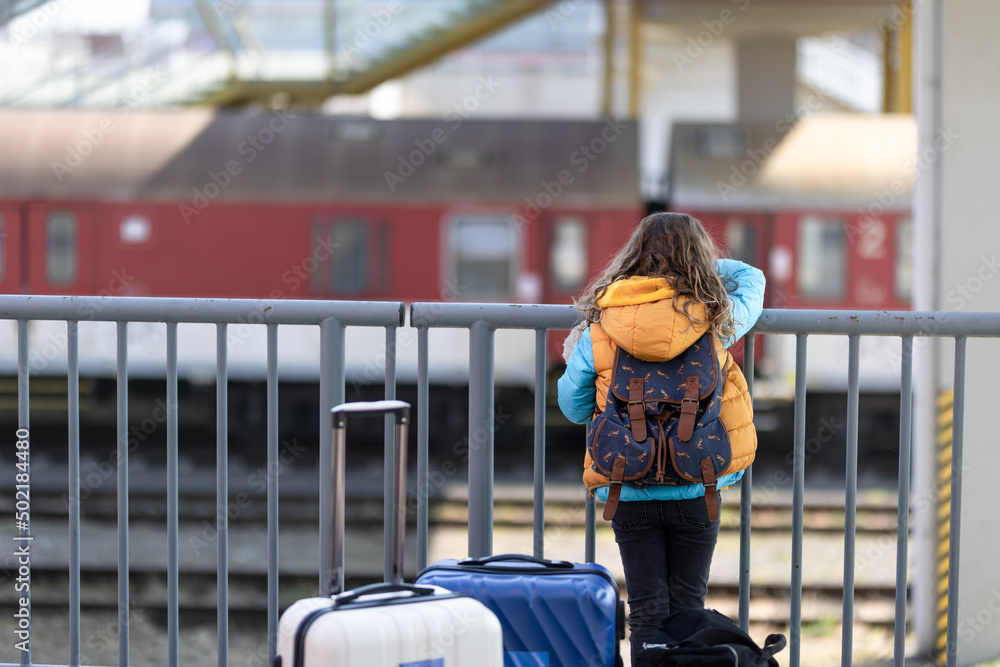 Wall mural Rear view of Ukrainian immigrant child with luggage waiting at train station, Ukrainian war concept.