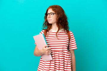 Fototapeta premium Student teenager redhead girl isolated on blue background looking to the side
