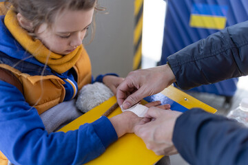 Volunteer helping Ukrainian refugee child at train station, giving plaster to injured hand.