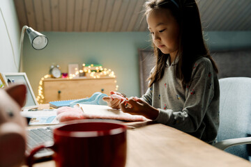 Asian girl doing homework with laptop while sitting at table
