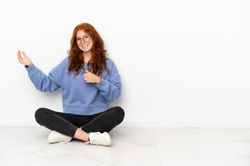 Teenager redhead girl sitting on the floor isolated on white background making guitar gesture