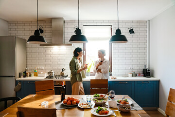 Mature two women laughing and drinking wine while having dinner