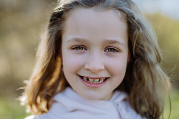 Fototapeta premium A portrait of pretty child girl standing in summer park looking in camera smiling happily.