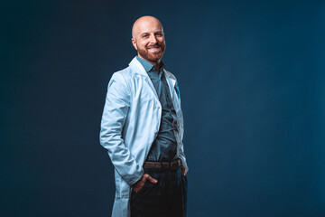 Photo of cheerful doctor with beard posing and smiling at camera with blue background and medical...