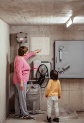 Senior woman with little child in nuclear fallout shelter built in basement of building showing him rules how to use bombshelter