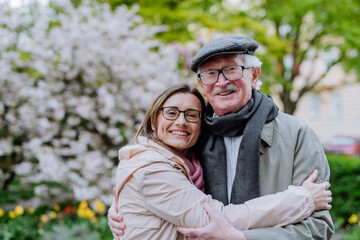 Adult daughter hugging her senior father outdoors in park on spring day.