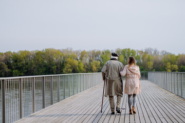 Rear view of senior man with daughter outdoors on a walk on pier by river. - Powered by Adobe