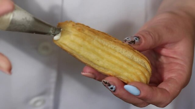 A woman fills eclairs with cream from a pastry bag. Cooking cakes from choux pastry with cream. Close-up