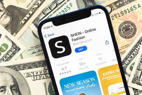 Shein fashion shopping app logo on mobile phone screen. Business background with dollar money banknotes photo