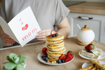 A woman reads a mother's day gift card from her child. Breakfast surprise: pancakes with strawberries and blueberries.
