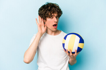 Young caucasian man playing volleyball isolated on blue background trying to listening a gossip.