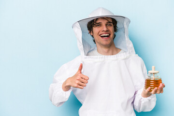 Young caucasian beekeeper man isolated on blue background smiling and raising thumb up