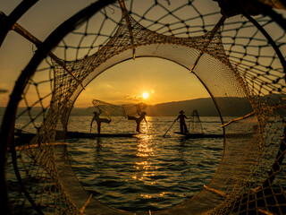 Silhouette of three traditional Burmese fishermen on Inle Lake at sunset in Myanmar