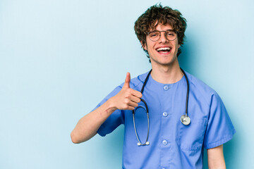 Young caucasian nurse man isolated on blue background smiling and raising thumb up