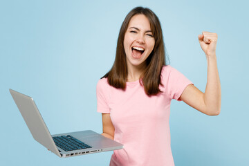 Young freelancer happy woman 20s wearing pink t-shirt hold use work on laptop pc computer do winner...