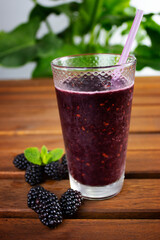 glass cup with blackberry smoothie with blacberry slices on wooden table