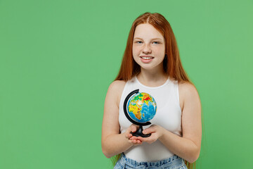Little redhead kid smiling happy fun cool girl 12-13 years old wearing white tank shirt hold in hands Earth world globe isolated on plain green background studio portrait. Childhood lifestyle concept.