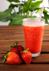 glass cup with strawberry smoothie with strawberry slices on wooden table