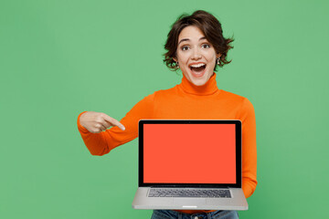 Young smiling happy woman 20s wear orange turtleneck hold use work point finger on laptop pc...