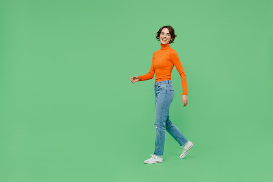 Full body young smiling happy cool fun woman 20s wearing casual orange turtleneck walk going strolling isolated on plain pastel light green color background studio portrait. People lifestyle concept.