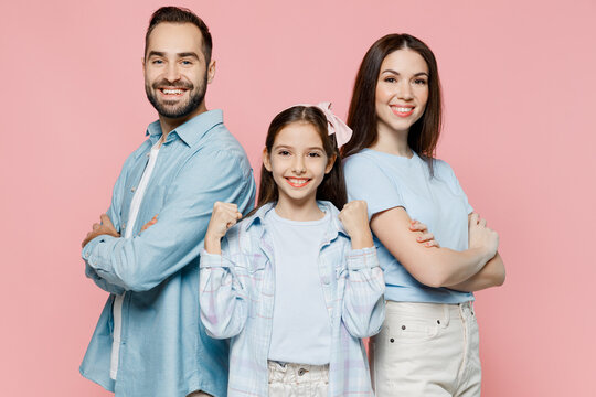 Young fun parents mom dad with child kid daughter teen girl in blue clothes hold hands crossed folded do winner gesture isolated on plain pastel light pink background. Family day parenthood concept.