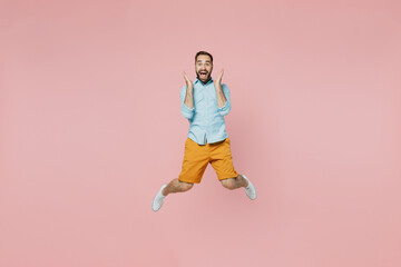 Full body young excited overjoyed winner fun cool happy man 20s wearing classic blue shirt jump high hold face isolated on plain pastel light pink background studio portrait. People lifestyle concept.