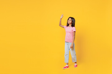 Full body smiling happy fun little kid girl of African American ethnicity 12-13 years old wearing pink t-shirt walking go waving hand isolated on plain yellow background. Childhood lifestyle concept.