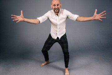 A bald guy in a white shirt and dark plaid pants throws up his hands on a gray background.