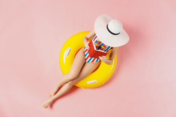 Top view full size young woman in striped swimsuit lies on inflatable rubber ring pool read book...