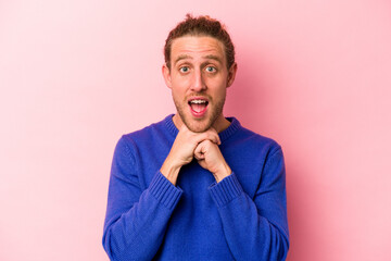 Young caucasian man isolated on pink background praying for luck, amazed and opening mouth looking to front.