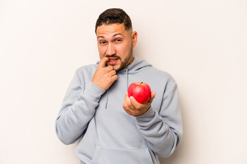 Hispanic man holding an apple isolated on white background biting fingernails, nervous and very anxious.