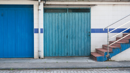 Puertas de garage en diferentes tono de azul en calle con escalera
