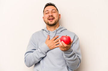 Hispanic man holding an apple isolated on white background laughs out loudly keeping hand on chest.