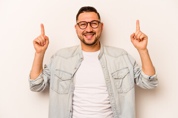 Young hispanic man isolated on white background indicates with both fore fingers up showing a blank...