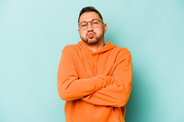 Young hispanic man isolated on blue background blows cheeks, has tired expression. Facial expression concept.