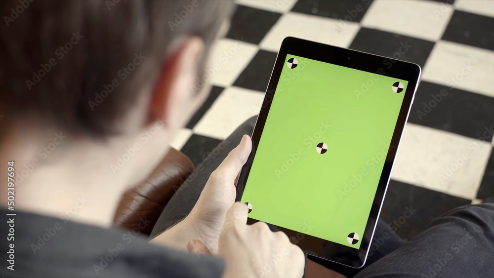 Poster Close-up of man holding tablet and touching green screen. Stock fooatge. Young freelancer uses tablet to work or create projects. Tablet with green screen to insert