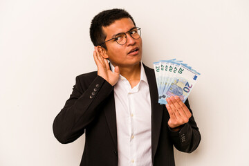 Young hispanic business man holding banknotes isolated on white background trying to listening a gossip.