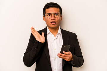 Young business hispanic man holding mobile phone isolated on white background surprised and shocked.