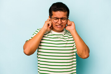 Young hispanic man isolated on blue background covering ears with hands.
