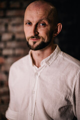 Portrait of a bald man with a beautiful beard in a white shirt on a brick background