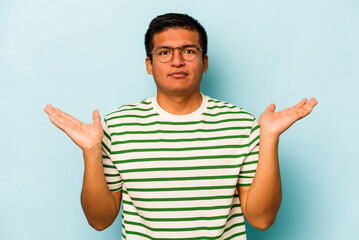Fototapeta premium Young hispanic man isolated on blue background makes scale with arms, feels happy and confident.
