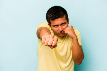 Young hispanic man isolated on blue background throwing a punch, anger, fighting due to an...