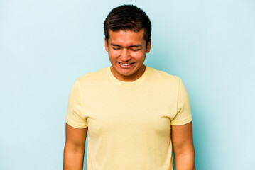 Obraz premium Young hispanic man isolated on blue background laughs and closes eyes, feels relaxed and happy.