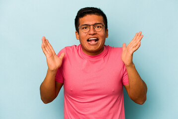Fototapeta premium Young hispanic man isolated on blue background receiving a pleasant surprise, excited and raising hands.